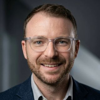 Michael Carrico smiling, wearing glasses and a navy jacket.